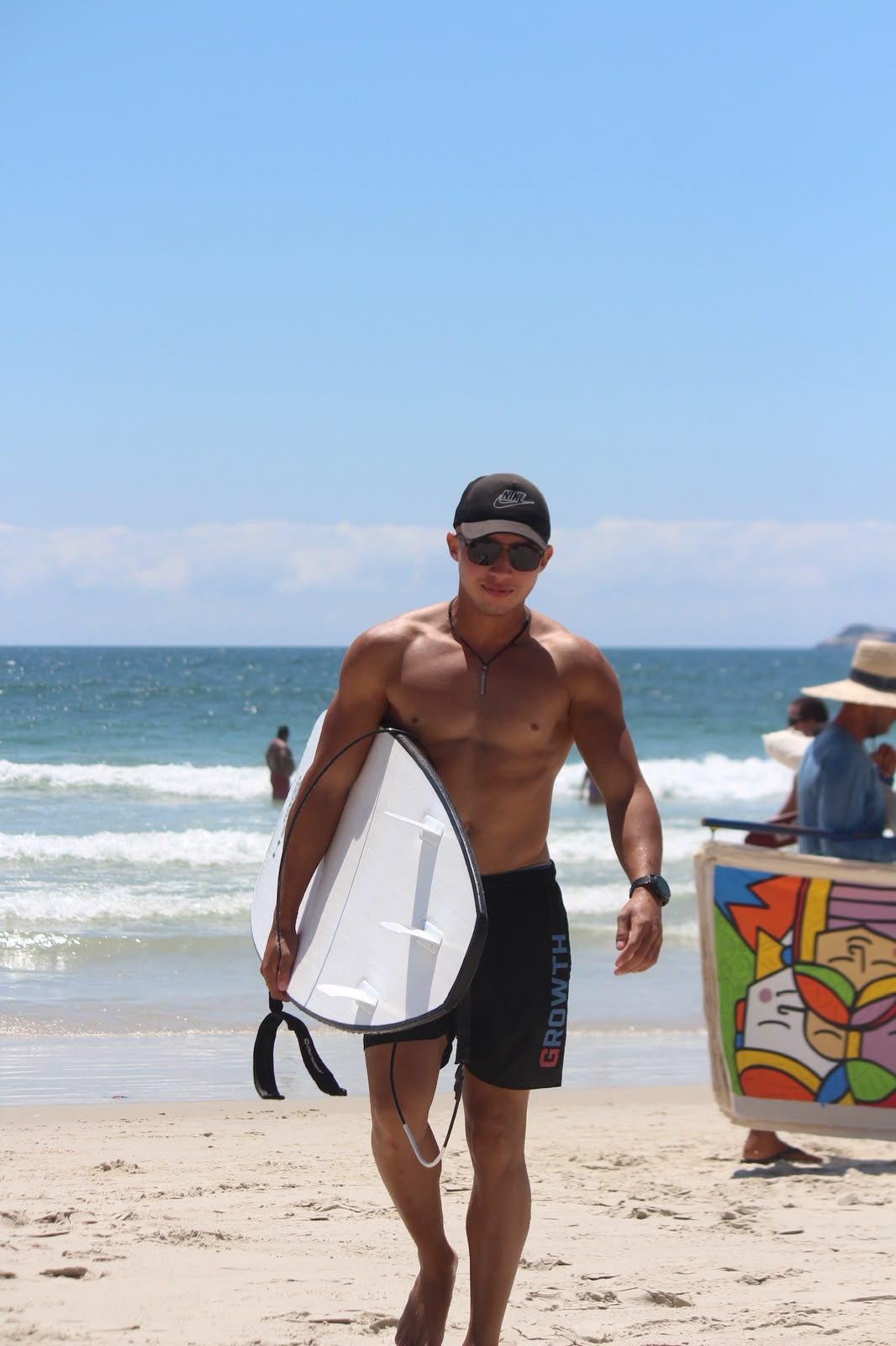 Cauê Aquino sorrindo na praia com uma prancha